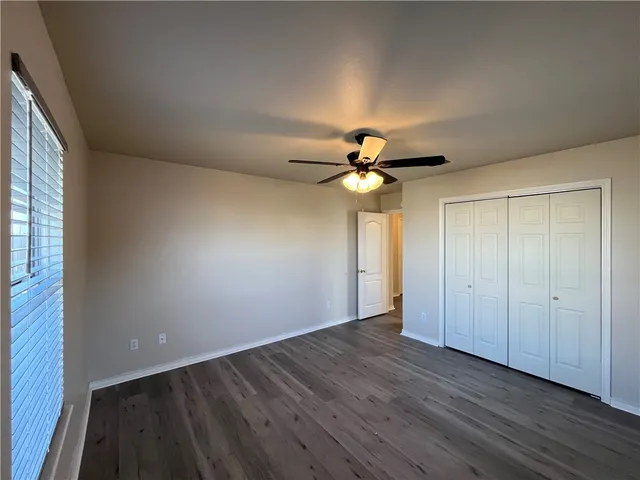 an empty room with wooden floor fan and windows