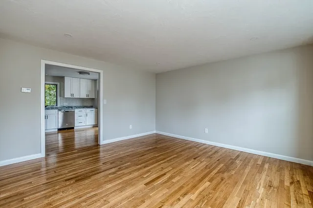 a view of empty room with wooden floor and kitchen
