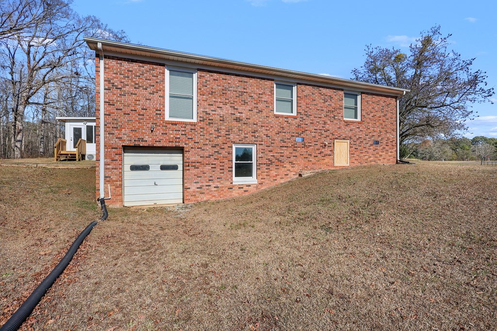 202 Wilton Road Abbeville, SC 29620 - Photo 8 of 35 This brick structure features a functional garage, set against a natural landscape with mature trees.