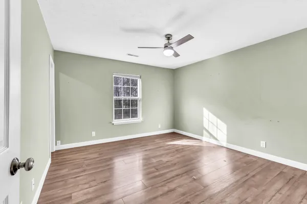 an empty room with wooden floor fan and windows