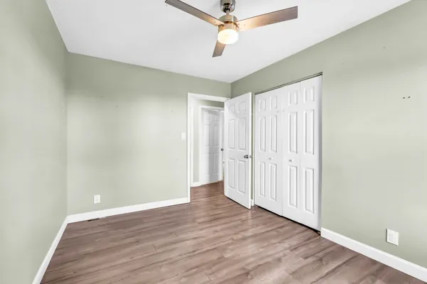 an empty room with wooden floor fan and windows