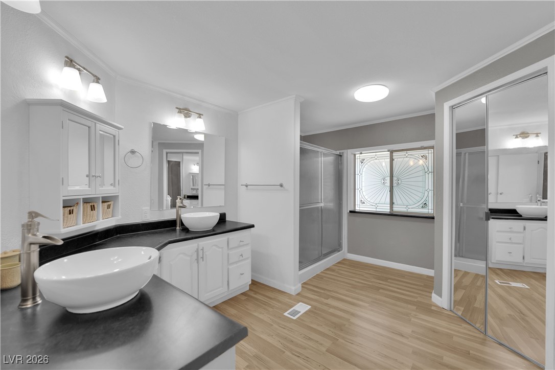 5550 Vicki Ann Road Pahrump, NV 89048 - Photo 18 of 44 Bathroom featuring two vanities, crown molding, light wood-style flooring, and a stall shower