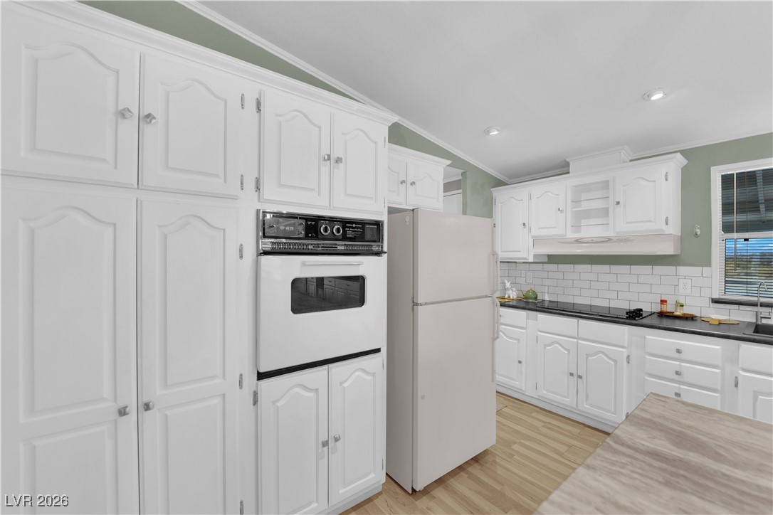 5550 Vicki Ann Road Pahrump, NV 89048 - Photo 30 of 44 Kitchen featuring white cabinetry, light wood-style floors, white appliances, backsplash, and crown molding