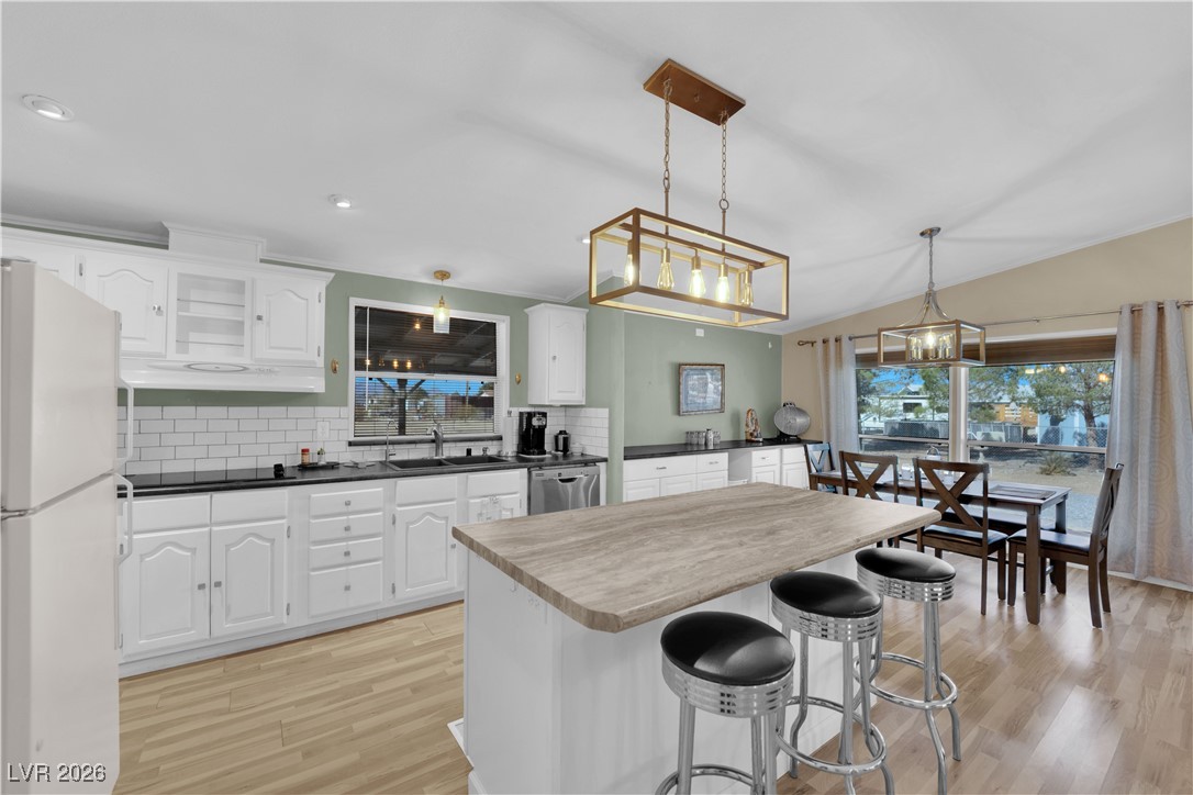 5550 Vicki Ann Road Pahrump, NV 89048 - Photo 31 of 44 Kitchen with freestanding refrigerator, white cabinets, light wood-style floors, decorative backsplash, and a kitchen breakfast bar