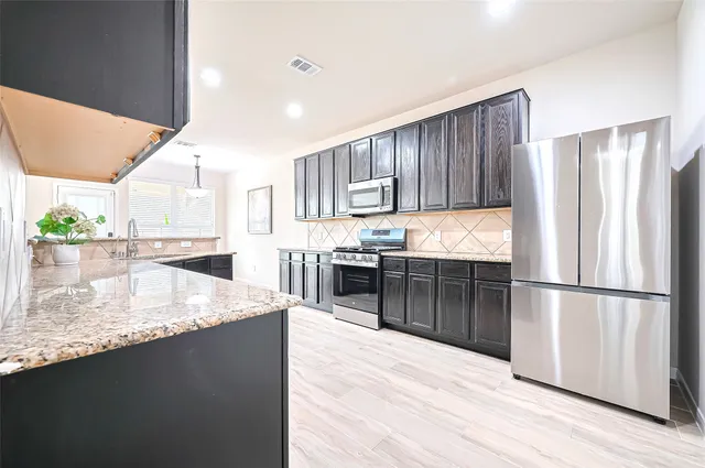 a kitchen with stainless steel appliances granite countertop a refrigerator a sink dishwasher a stove and a refrigerator with wooden floor