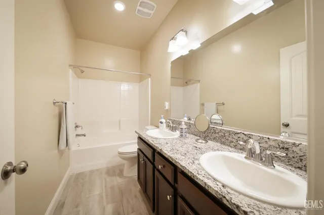 a bathroom with a granite countertop sink a toilet a large mirror and shower