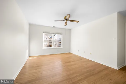 an empty room with wooden floor ceiling fan and windows
