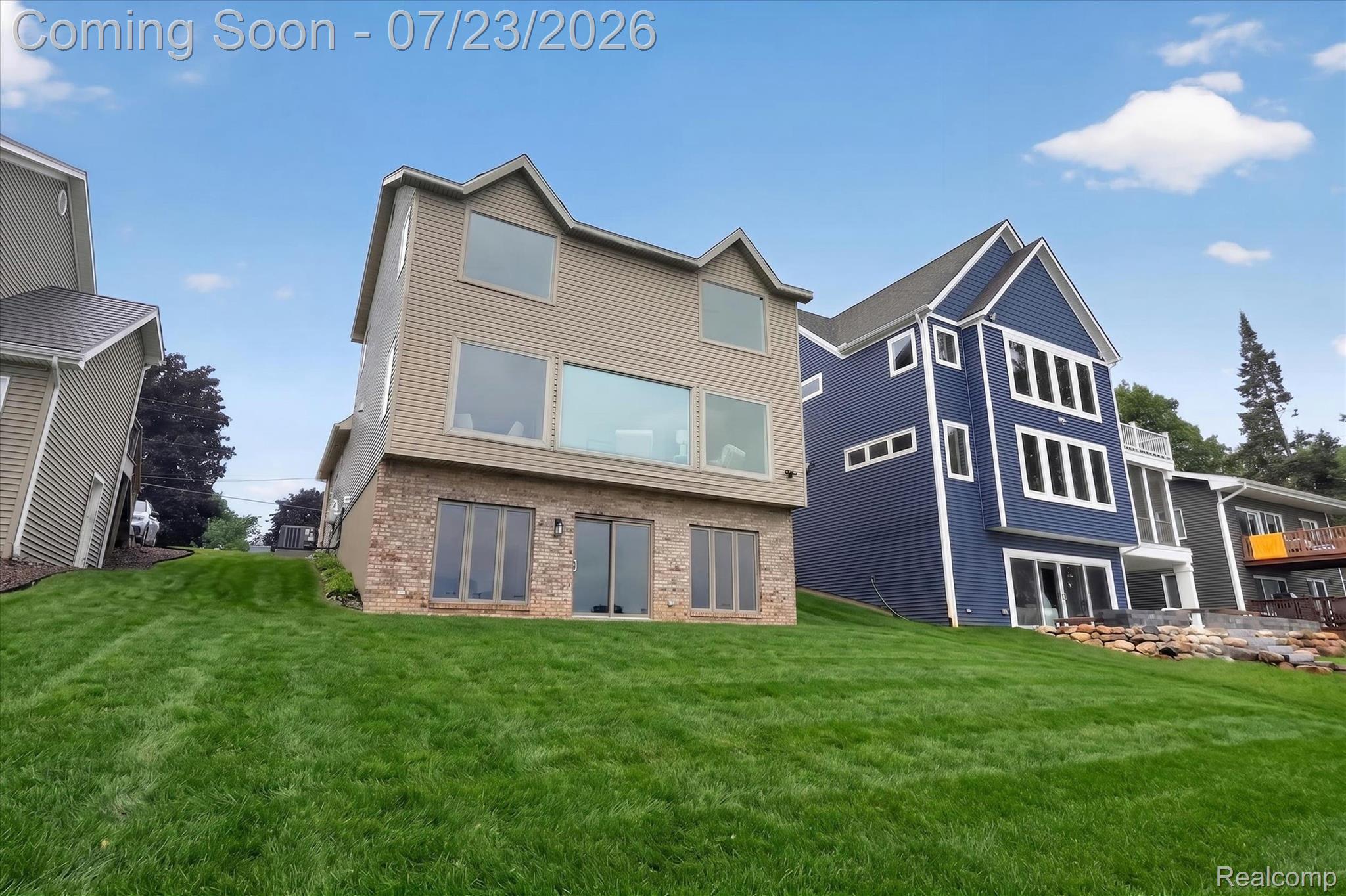 3429 Rolston Road Fenton, MI 48430 - Photo 47 of 62 Expansive grassy yard leading to a contemporary residence featuring multiple large windows, a brick base, and a walk-out lower level with sliding glass doors