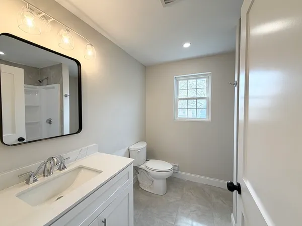 a bathroom with a toilet a sink a mirror and a window