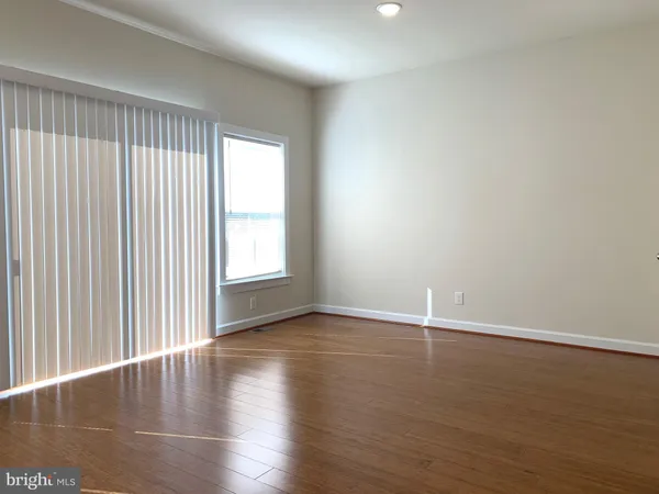 an empty room with wooden floor and windows with curtains