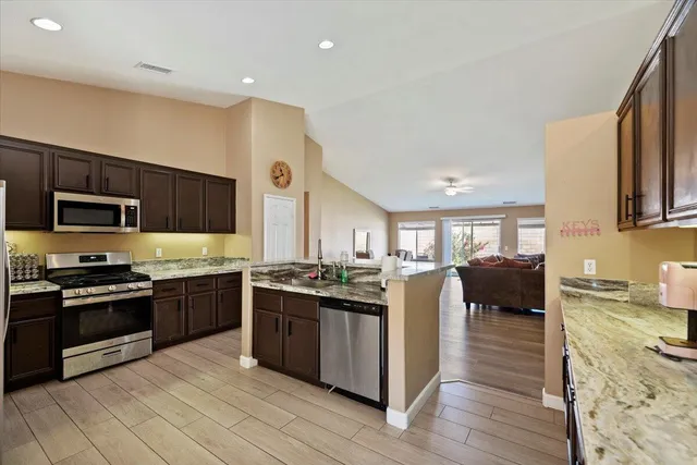 a kitchen with stainless steel appliances granite countertop a stove top oven a sink dishwasher a dining table and chairs with wooden floor