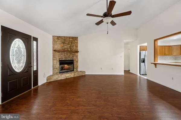 a view of an empty room with wooden floor a ceiling fan and a fireplace