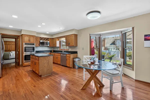 a open kitchen with stainless steel appliances granite countertop a refrigerator a stove top oven and a dining table with wooden floor