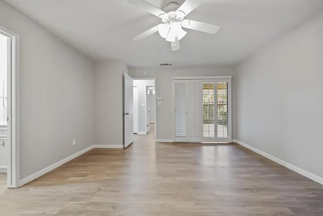 a view of an empty room with chandelier fan and wooden floor