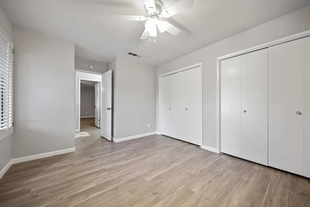 a view of an empty room with wooden floor and a ceiling fan