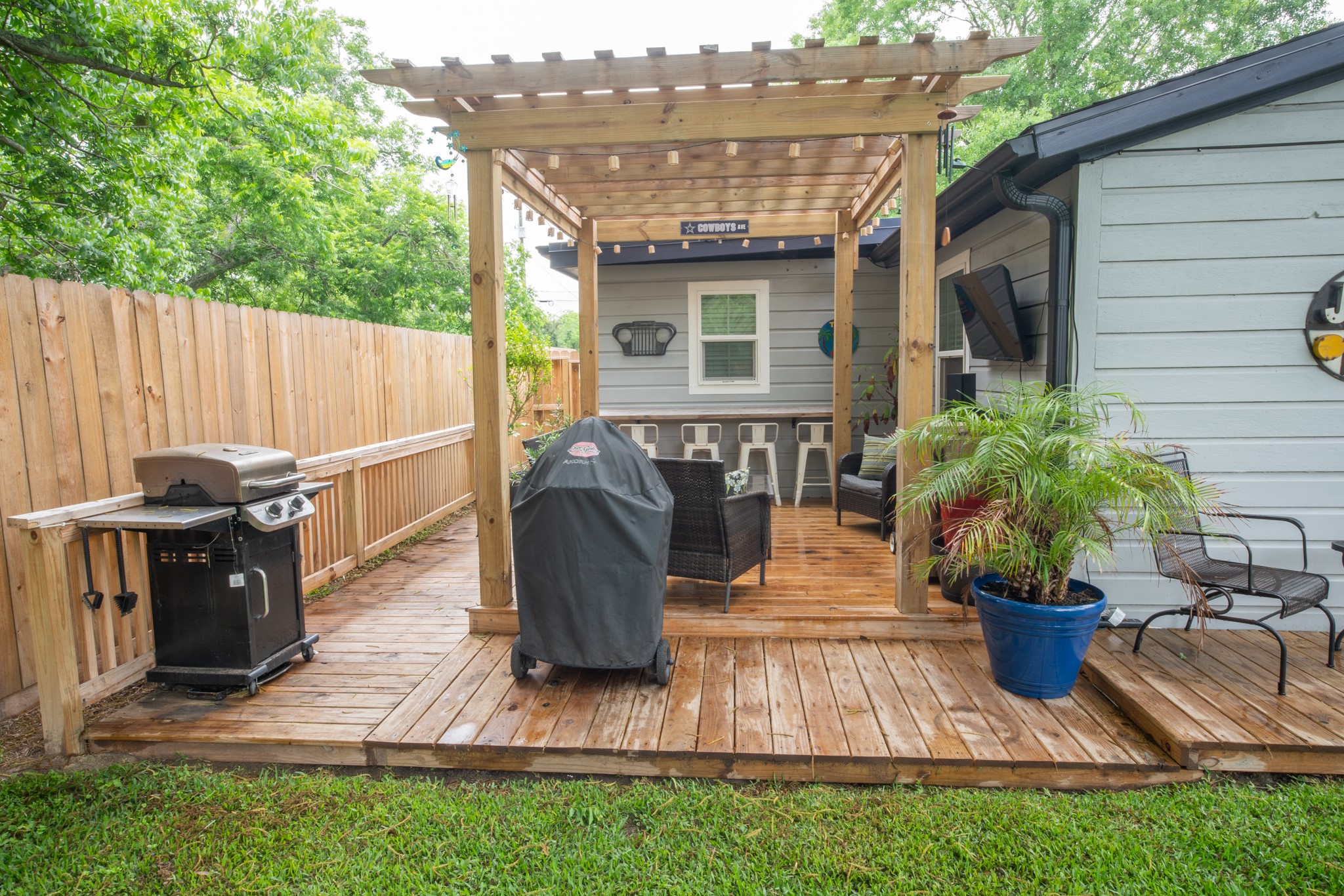 846 South Anderson Street Angleton, TX 77515 - Photo 23 of 30 This photo showcases a cozy backyard patio with a wooden deck, pergola, and seating area. There's a grill for outdoor cooking, surrounded by lush greenery and a privacy fence, perfect for relaxing or entertaining.