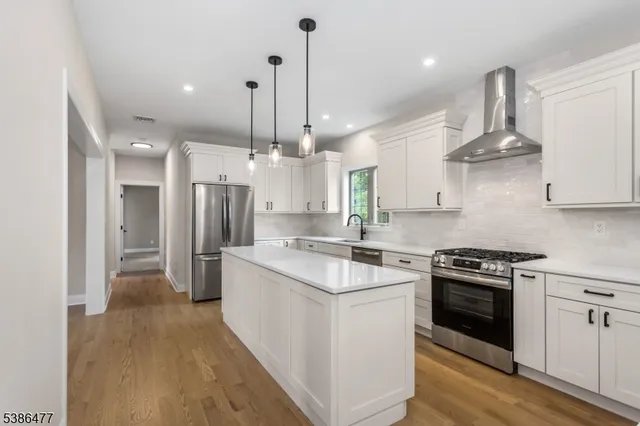 a kitchen with stainless steel appliances kitchen island a stove a refrigerator a sink and a wooden floor