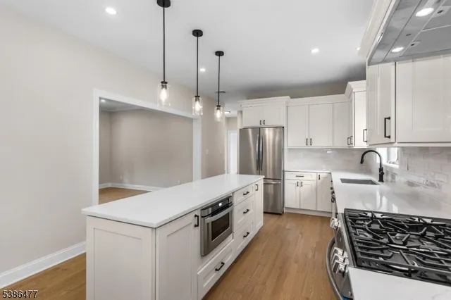 a kitchen with stainless steel appliances a stove a sink a refrigerator and white cabinets with wooden floor