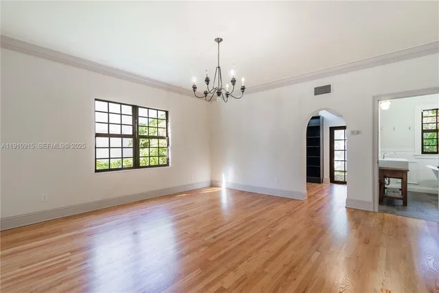 an empty room with wooden floor chandelier and windows