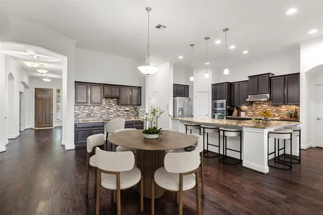 a kitchen with kitchen island granite countertop a dining table chairs wooden floor cabinets and stainless steel appliances