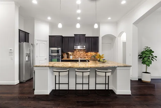 a kitchen with kitchen island granite countertop wooden floor and refrigerator