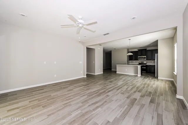 a view of empty room with wooden floor and kitchen view