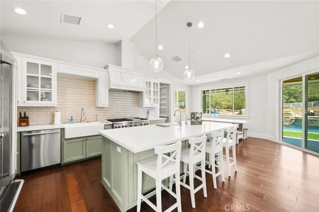 a kitchen with stainless steel appliances granite countertop a stove top oven a sink dishwasher a dining table and chairs with wooden floor