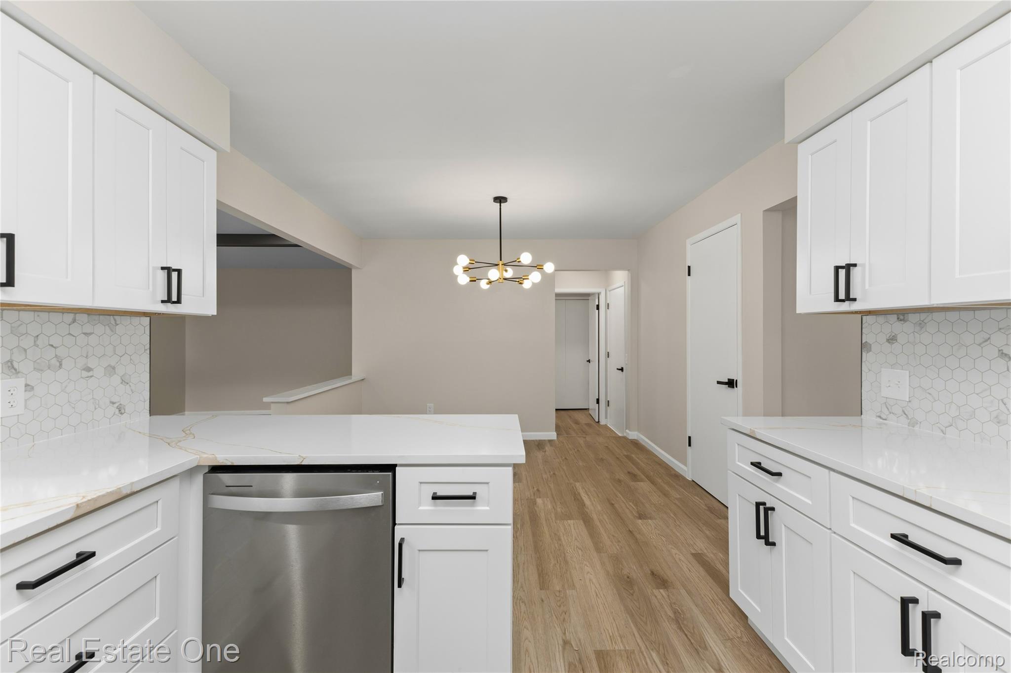 25695 Branchaster Road Farmington, MI 48336 - Photo 14 of 58 White cabinetry with matte black hardware, hexagonal tile backsplash, light-toned wood-finish flooring, and a modern chandelier