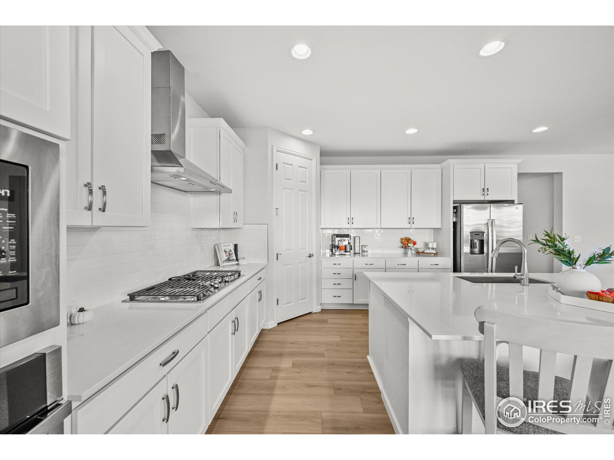 950 Rustling Street Windsor, CO 80550 - Photo 4 of 49 a kitchen with stainless steel appliances kitchen island granite countertop a stove a sink a refrigerator and white cabinets with wooden floor