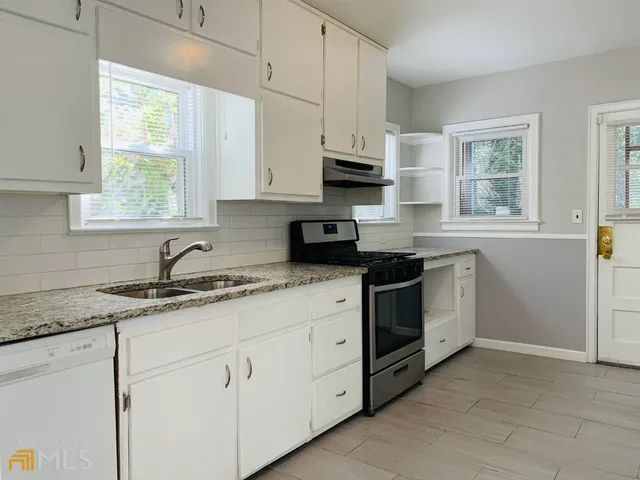 a kitchen with granite countertop white cabinets white stainless steel appliances a sink and a window