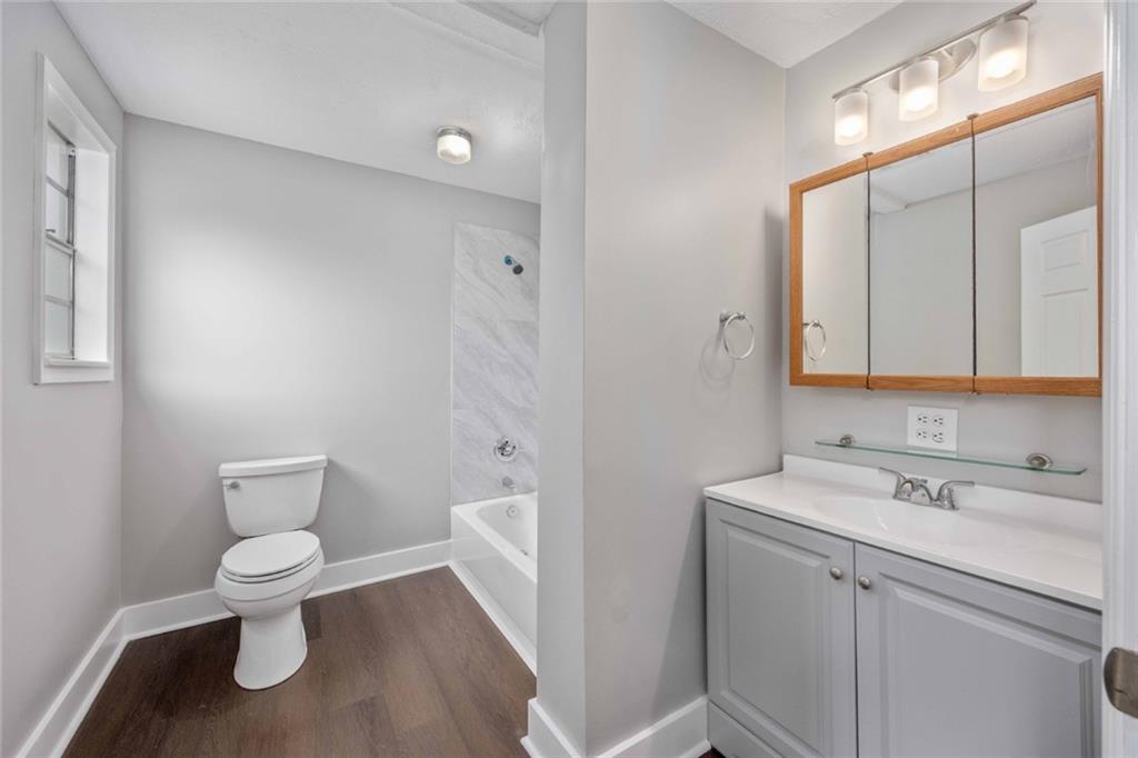 9 Spies Road Fort Mitchell, AL 36856 - Photo 16 of 23 Bathroom featuring a white vanity with integrated sink, a wood-framed medicine cabinet, a full bathtub with tiled surround, wood-finish flooring, and a white toilet