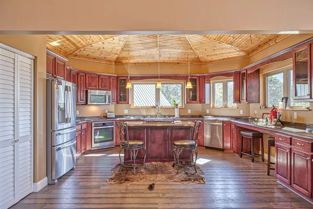 a kitchen with stainless steel appliances granite countertop a refrigerator a sink dishwasher a dining table and chairs with wooden floor