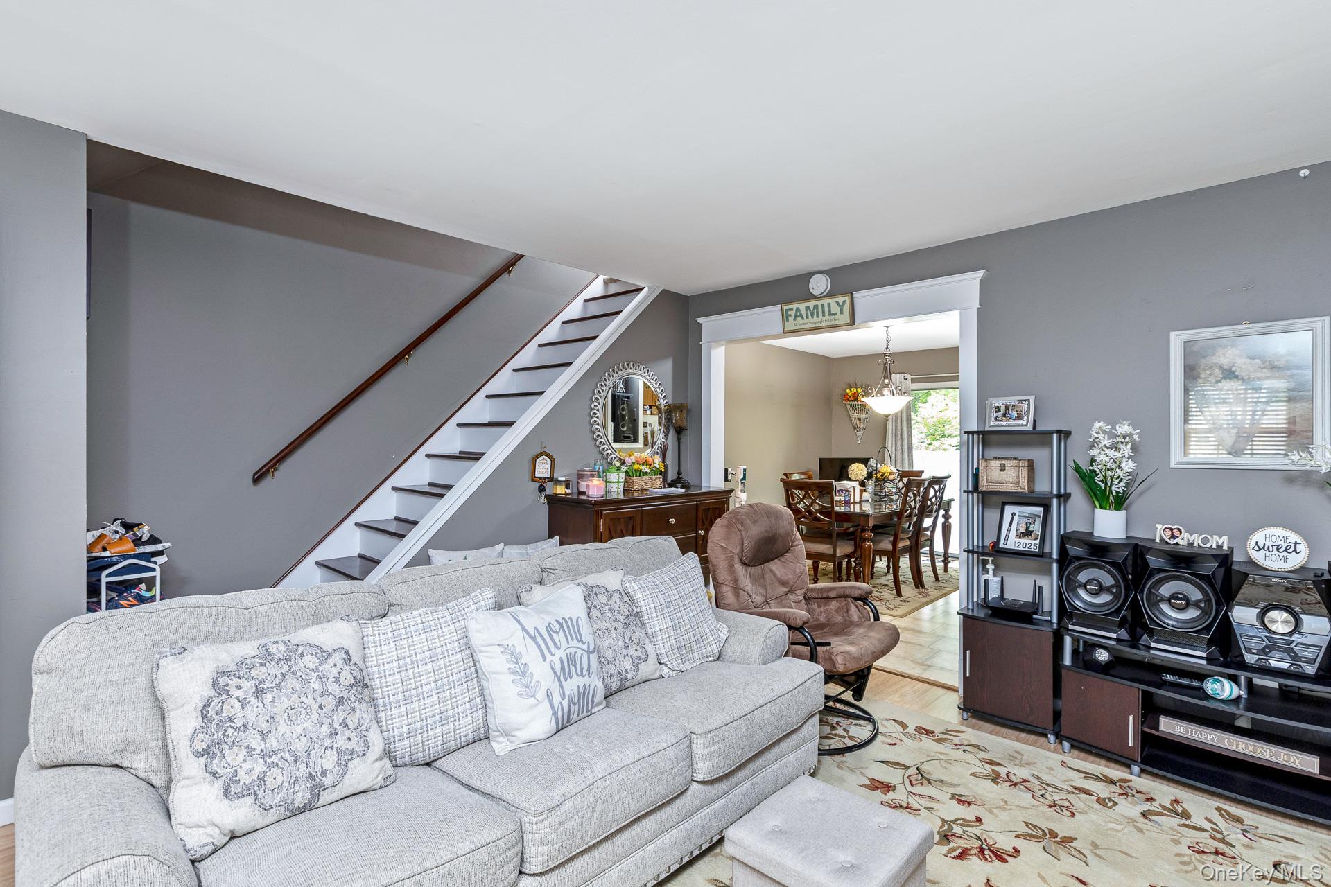 17 Stone Commons Yaphank, NY 11980 - Photo 12 of 31 Living area featuring a staircase with dark treads and a wood handrail, light gray walls, and a broad archway opening to a dining space