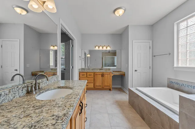 a bathroom with a granite countertop tub double vanity sink and a large mirror