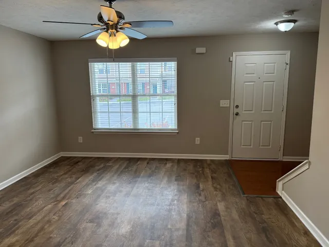 an empty room with wooden floor chandelier fan and windows