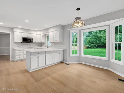 a large white kitchen with granite countertop a stove a sink dishwasher and white cabinets with wooden floor