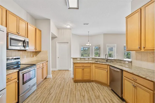 a kitchen with stainless steel appliances granite countertop a stove a sink dishwasher and a refrigerator with wooden floor