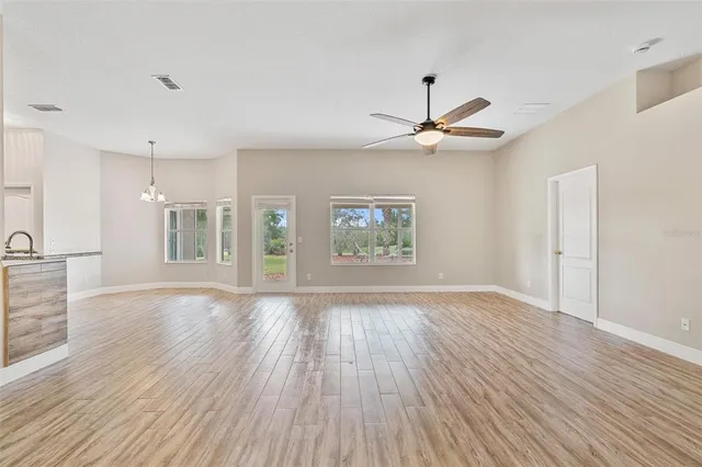 a view of an empty room with wooden floor and a kitchen