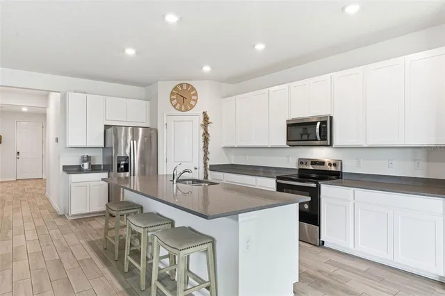 a kitchen with stainless steel appliances a stove top oven a sink a refrigerator white cabinets and wooden floor