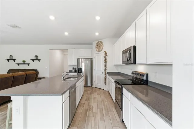 a kitchen with granite countertop a refrigerator a stove a sink and white cabinets with wooden floor