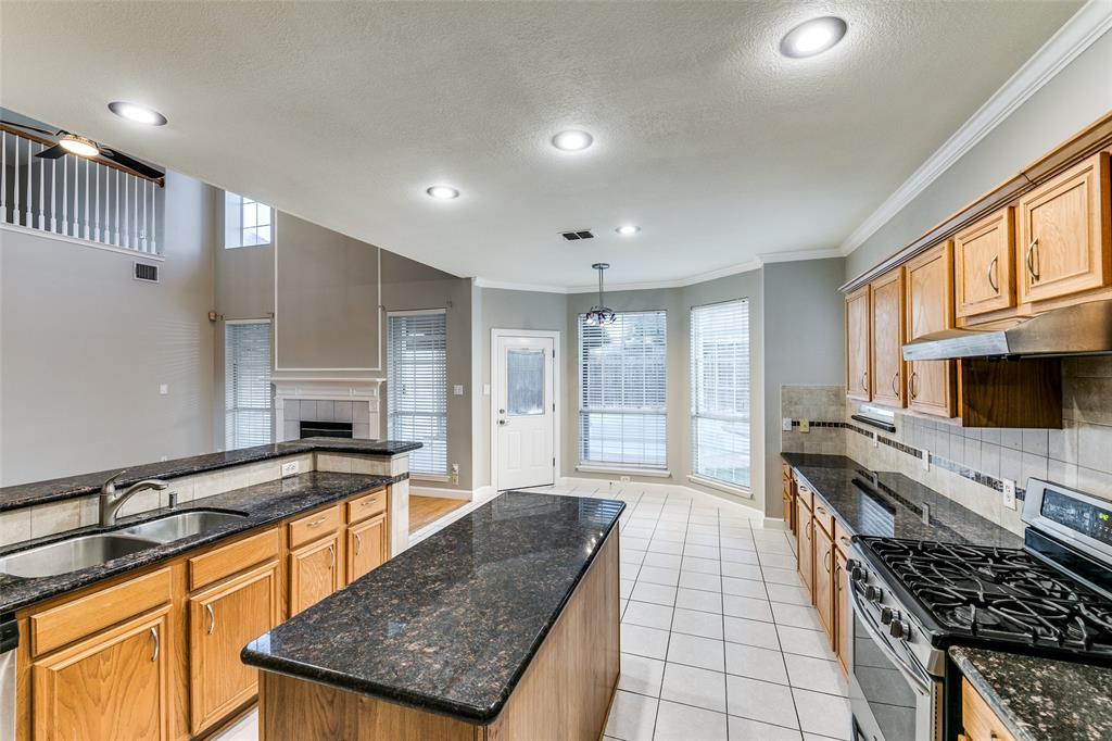 4532 Crown Ridge Drive Plano, TX 75024 - Photo 8 of 25 Open-concept kitchen featuring wood cabinetry, dark stone countertops, stainless steel appliances, a center island, and tile flooring