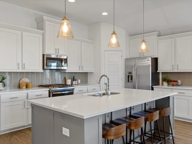 a large white dining hall with stainless steel appliances kitchen island granite countertop a table chairs and a refrigerator