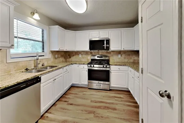 a kitchen with granite countertop a sink stainless steel appliances and white cabinets