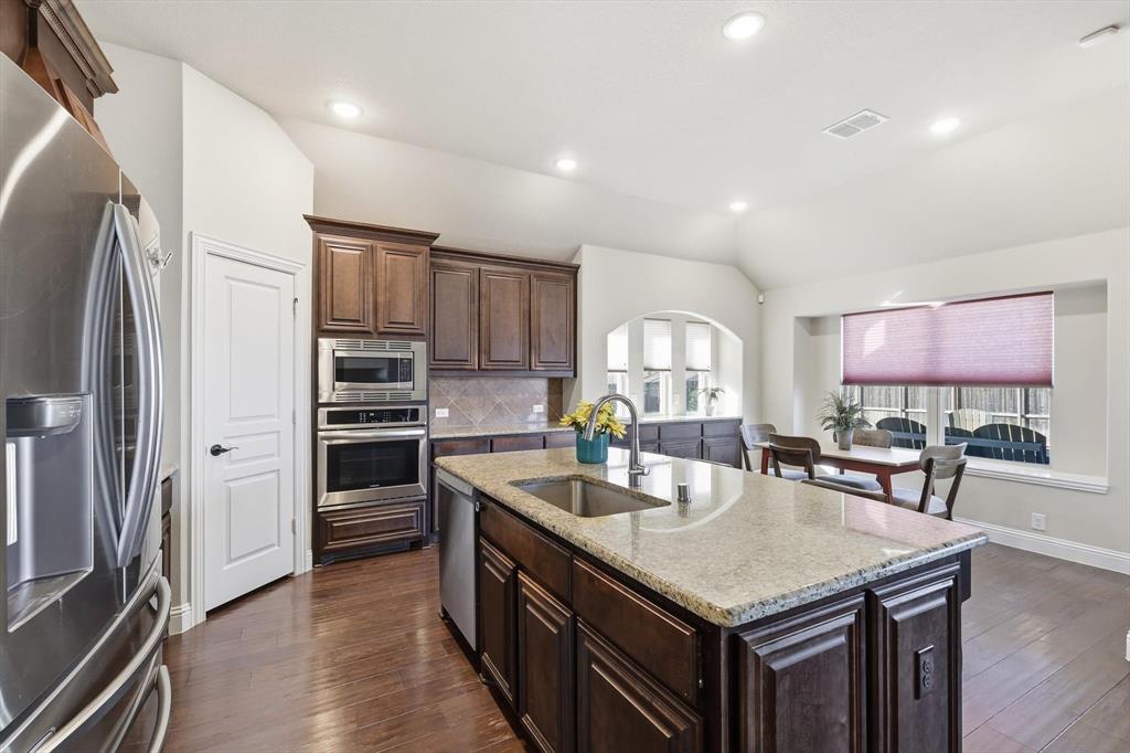 4609 Jasmine Trail Midlothian, TX 76065 - Photo 17 of 34 Kitchen featuring dark brown cabinetry, appliances with stainless steel finishes, tasteful backsplash, light stone counters, and dark wood-style floors