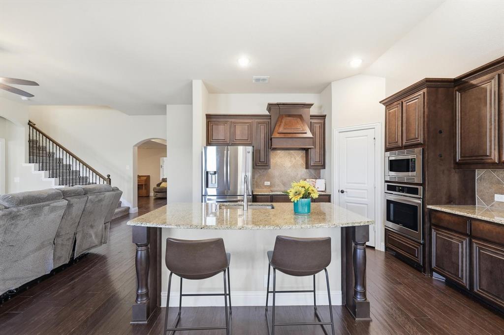 4609 Jasmine Trail Midlothian, TX 76065 - Photo 18 of 34 Kitchen featuring light stone counters, a breakfast bar, dark brown cabinetry, tasteful backsplash, and stainless steel appliances