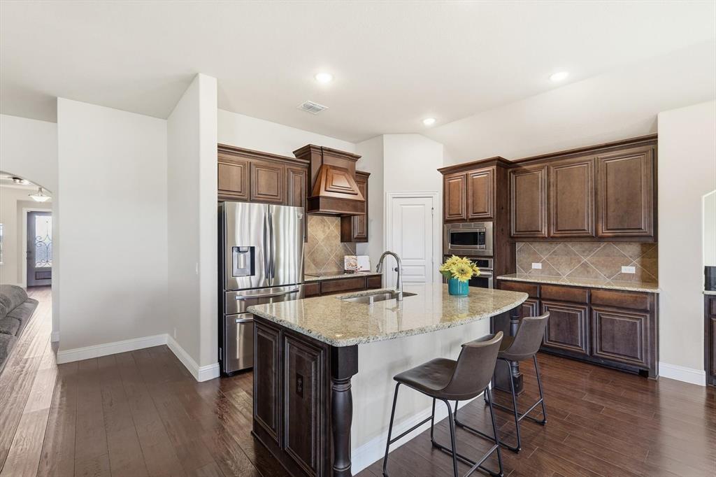 4609 Jasmine Trail Midlothian, TX 76065 - Photo 4 of 34 Stainless appliances, light stone counters, dark brown cabinetry, dark wood-style flooring, and premium range hood