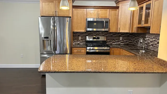 a kitchen with stainless steel appliances granite countertop a refrigerator a stove and a sink with wooden cabinets