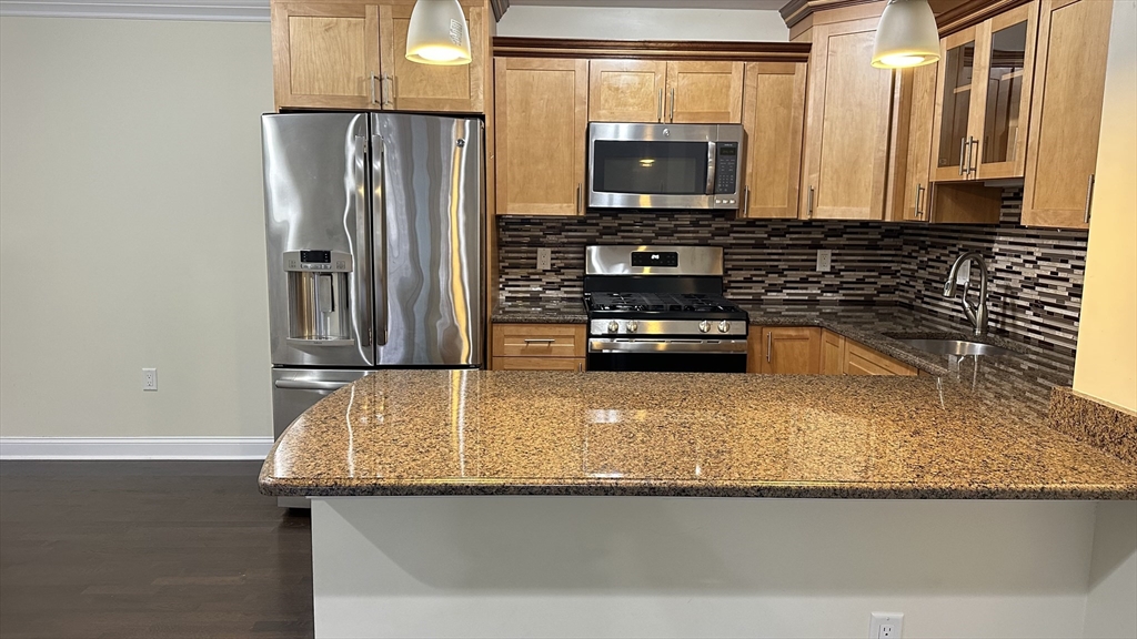 39 Fayette Street, Unit 102 Quincy, MA 02171 - Photo 7 of 24 a kitchen with stainless steel appliances granite countertop a refrigerator a stove and a sink with wooden cabinets