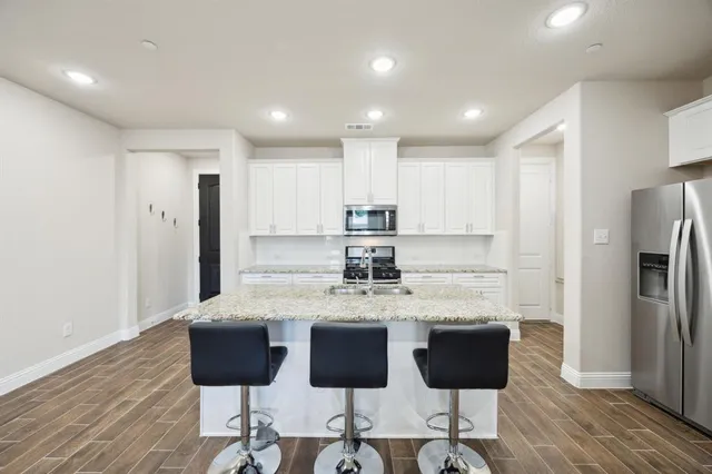 a kitchen with stainless steel appliances granite countertop a refrigerator a stove a sink and white cabinets with wooden floor