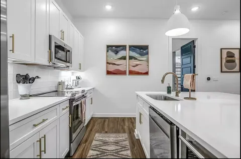 a kitchen with stainless steel appliances granite countertop a sink stove oven and white cabinets with wooden floor